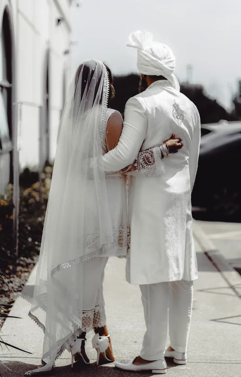 A bride in a veil and a groom in a turban walking away together